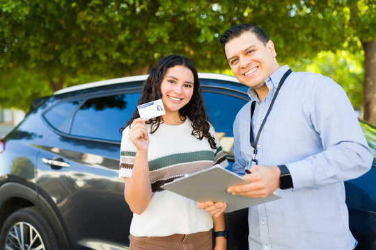 Portrait of a cheerful teenage student showing her new driver's license after passing her driving test with her instructor