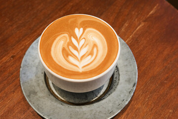 Close up of hot flower coffee art with milk coffee latte in a grey mug cup with plate