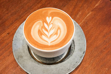 Close up of hot flower coffee art with milk coffee latte in a grey mug cup with plate