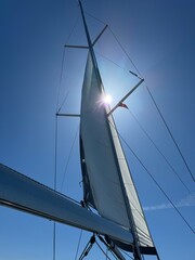Obraz premium Beautiful sailboat under a bright sun with clear blue sky backdrop