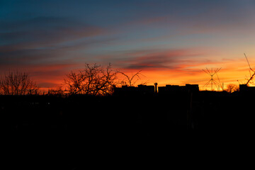 Sunrise. Silhouette of city buildings and bare tree branches at sunset with vibrant gradient sky. Landscape photography.