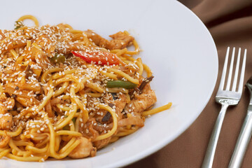 Oriental dish: Asian noodles with vegetables and chicken on a plate stands on the table.