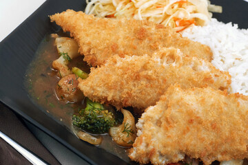 Oriental dish: crispy panko-coated chicken with vegetables, salad and rice on a plate stands on the table.