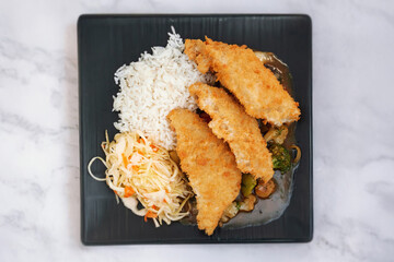 Oriental dish: crispy panko-coated chicken with vegetables, salad and rice on a plate stands on the table.