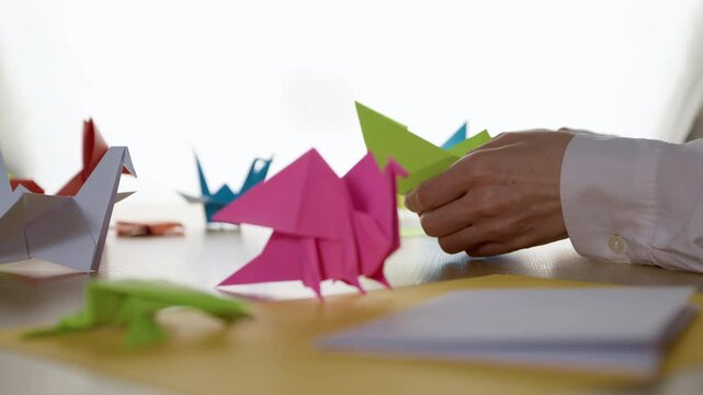 Woman's hands folding origami colored paper on table. Hobby, handmade and decor concept.