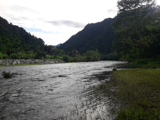 Stunning natural scenery of a mountain river flowing rapidly in the countryside. Perspective of the river landscape and the pristine nature with natural trees. Special Region of Aceh, Indonesia.