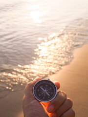 Close up hand holding compass with beach background in the sunset time © maybeiii