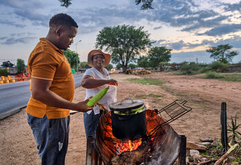 African street vendor, woman selling boiled corn to a young customer client , maize on the fire on...