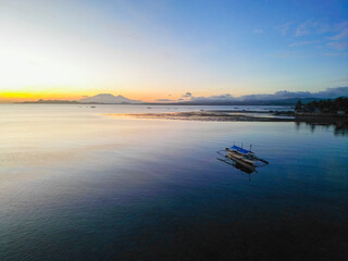 Tranquil Sunrise Over Calm Waters with Traditional Filipino Banca and Distant Mountains