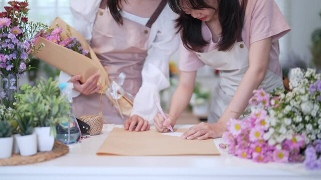 Two florists writing a greeting card to accompany a flower bouquet, adding a personal touch to their floral arrangement.