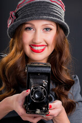 Vintage retro style portrait of beautiful smiling young woman holding an old film camera.