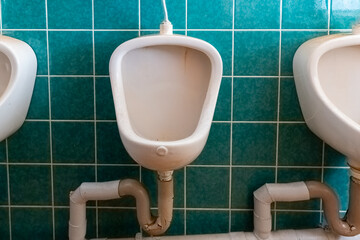 Urinals installed in a public restroom with vibrant turquoise tiles on the walls in daylight