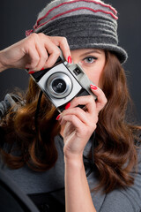 Vintage retro style portrait of a beautiful young woman holding an old film camera, watching and focusing on the viewer ready to take a photograph.