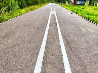 Obraz premium A deserted road in a rural area lined with grass and trees under a clear blue sky, inviting exploration and adventure