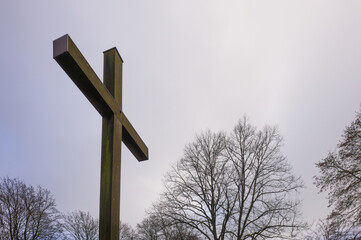 Large wooden cross standing tall against cloudy sky in winter