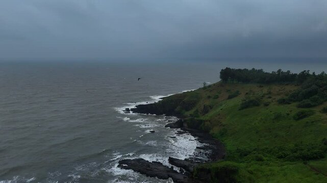 Drone pullback of a green cliffy beach with calm ocean and cloudy sky in Goa, Candolim, India