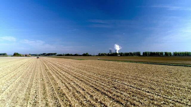 Drone flying low on a farmland, showcasing a Nuclear Energy Plant with smoke in the background
