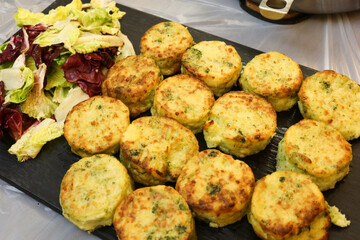 close up of baked fourteen homemade vegetable medallion made with mashed potato, broccoli, cheese, leek, onions and other vegetables on a black plate