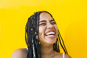 Portrait of a beautiful black woman with braids laughing with a yellow background