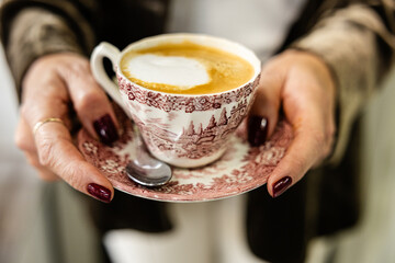 Woman holding a vintage coffee cup with frothy coffee.