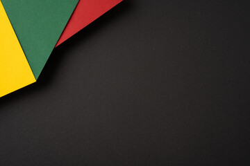 Abstract composition featuring red, green, and yellow paper sheets overlapping on a dark backdrop,...