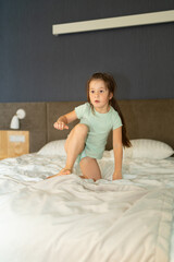 Fototapeta premium A small 6-year-old girl sits on her parents' bed in the bedroom, vertical photo.
