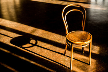 Elevated view of an old vintage cafe chair in a large empty room, with morning sunlight coming in through the windows and creating long dark shadows on floor.