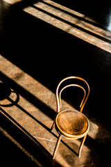 Elevated view of an old vintage cafe chair in a large empty room, with morning sunlight coming in through the windows and creating long dark shadows on floor.