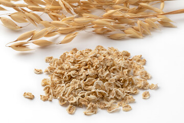 Heap of oat flakes and dried oat ears in the background close up on white background