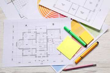 Designer's workplace with house plans, color palettes and stationery on light wooden table, flat lay