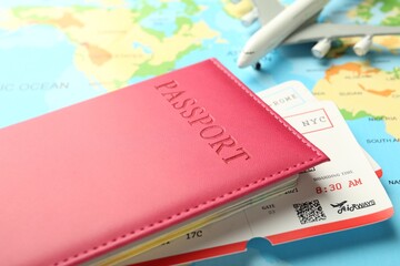Passport in pink cover, flight tickets and plane model on world map, closeup
