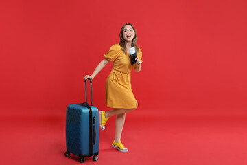 Happy traveller with suitcase, passport and ticket on red background