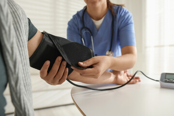 Doctor measuring patient's blood pressure at table indoors, closeup