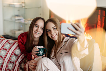 two teenage girls sisters holding cups of cocoa with marshmallows cozy atmosphere at home