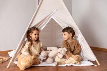 Happy little children siblings boy and girl sitting in a wigwam tent, playing and having fun at home. Children's room, childhood, games, imagination. High quality photo © Irina Mikhailichenko
