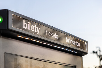 close-up of a ticket vending machine sign with illuminated text in three languages against a clear...