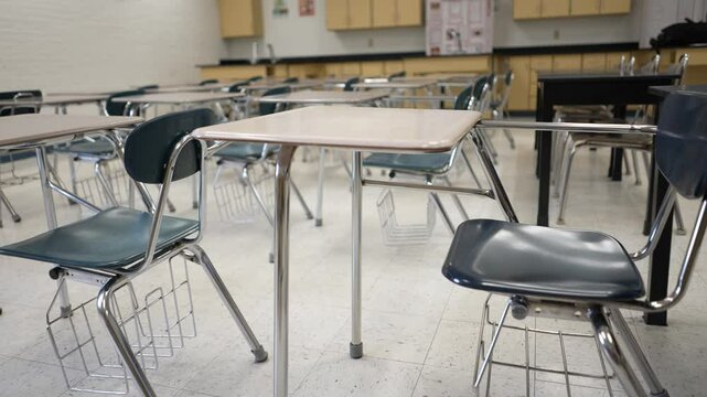 Desks and chairs are arranged neatly in an empty classroom, waiting for students to arrive and engage in learning activities. Sunshine streams through the windows.