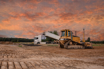 Obraz premium Crawler dozer an dump at a construction site in a quarry. Powerful modern equipment for earthworks. Construction site. Heavy bulldozer and dump or lorry at work. Building machines.