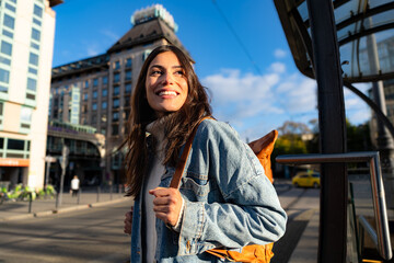 A curious woman carrying a denim jacket and a backpack walking through the busty city and looking...