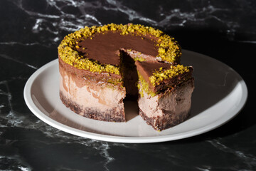 Sliced chocolate Dubai cheesecake with pistachio paste and kataifi dough filling covered in chocolate ganache on white plate. Black background. Indulgence, gourmet desserts, art of culinary