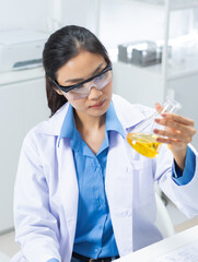 Professional Asian female scientist holds a flask analyzing chemical data, chemical reactions and documenting results on digital tablet in medical laboratory. Asian chemist works in a laboratory.