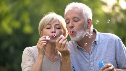 Fototapeta premium Happy Couple Blowing Bubbles in a Green Garden on a Sunny Day