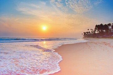 Colorful sunset viewed from the sea beach with soft waves and palm trees. Sri Lanka
