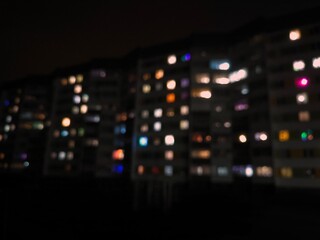Fototapeta premium Night urban landscape. Bright light of different colors from the windows of a multi-storey building, blurred. The lights are on in the windows of the houses at night