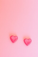 Two glossy red hearts displayed vertically on a soft pink background highlighting love and affection