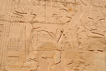 Naklejka premium Carved hieroglyphics and ancient reliefs etched into a sandstone temple wall, depicting historical Egyptian figures and symbols.