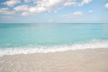 Gentle turquoise waves lapping onto a sandy shoreline under a bright sky, showcasing the tranquility of a tropical seaside.