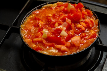 Tomatoes with sweet pepper and onion are fried in a pan in oil