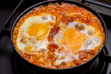 Shakshuka with tomatoes, peppers and onions is fried in a frying pan