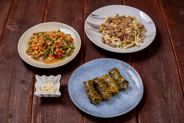 Couscous with vegetables, udon noodles with meat in spices and homemade dolma on a wooden table